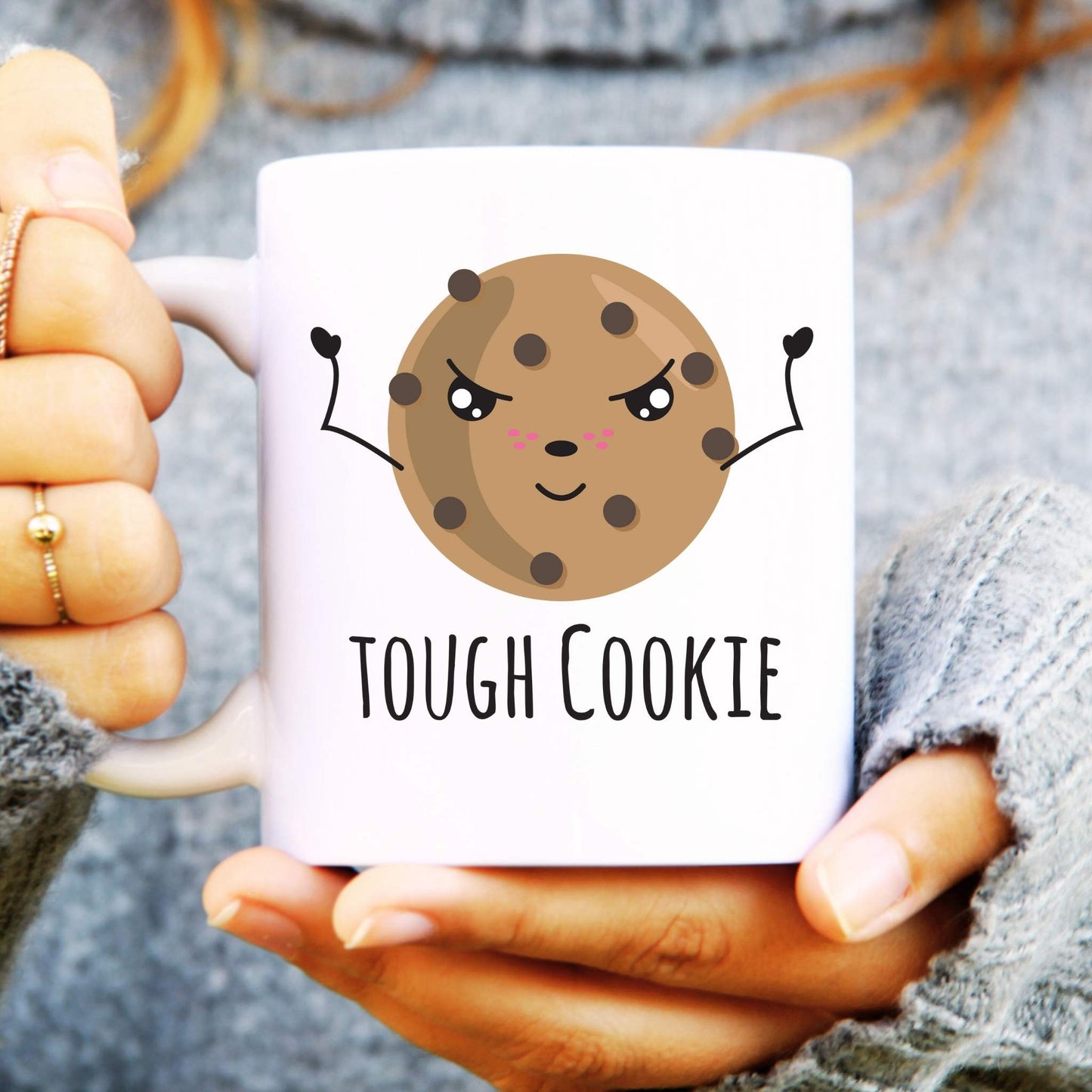 Mug with a cookie design and 'Tough Cookie' text held by hands.