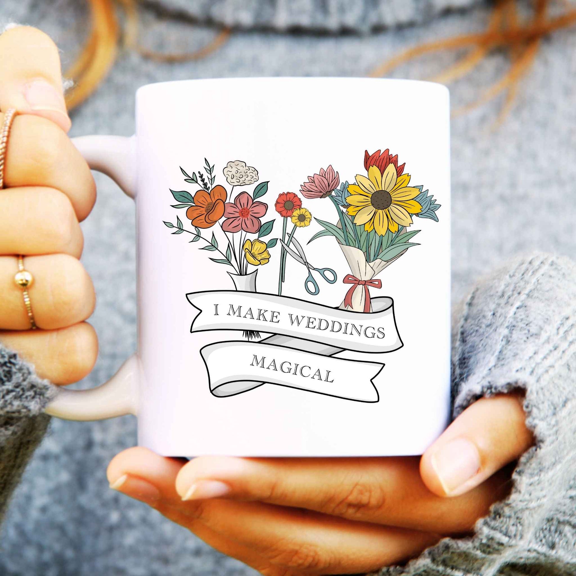 White mug with floral design and text says I make weddings magical held by a person