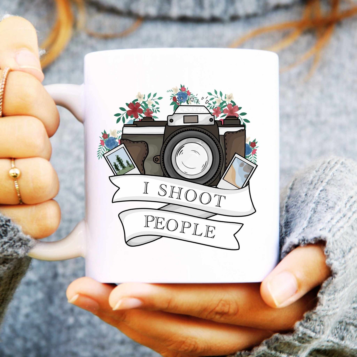 White mug with camera design and 'I shoot people' text held by a person.