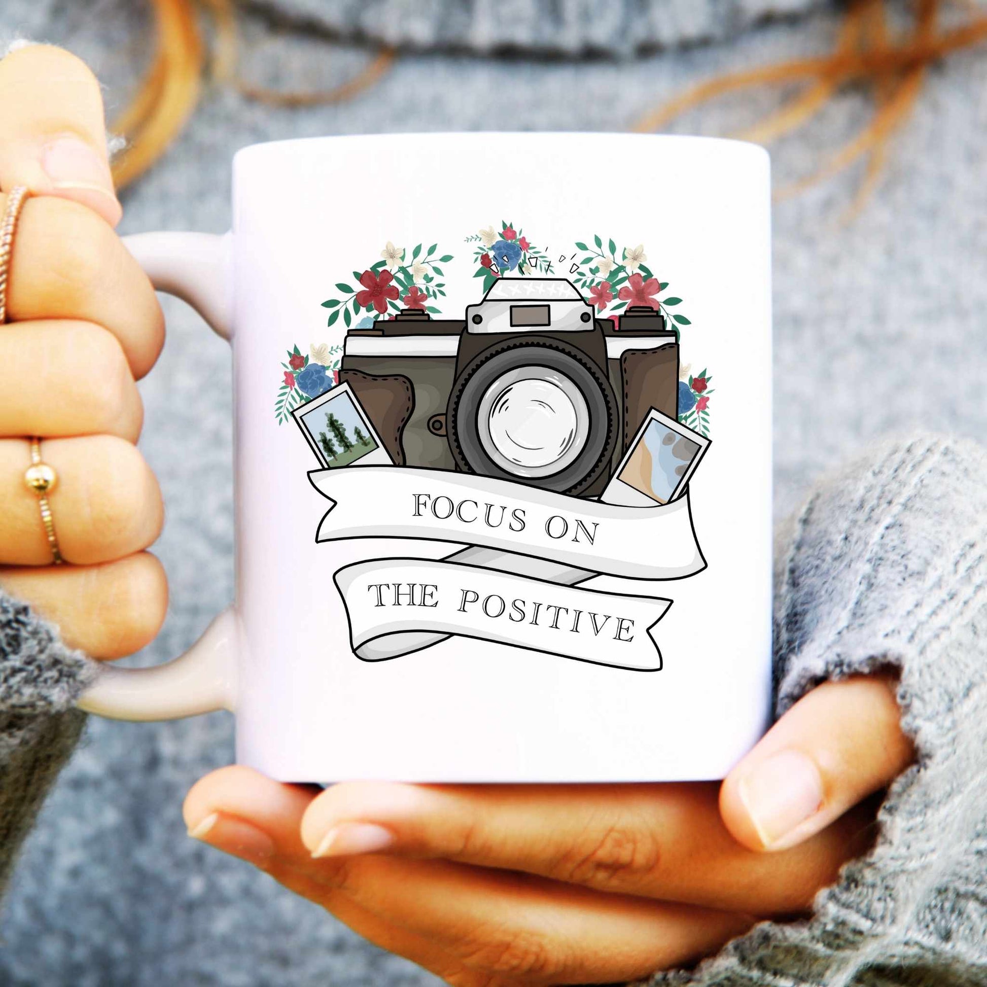 White mug with camera design and 'Focus on the Positive' text held by a person.