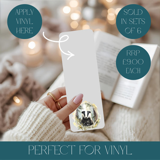 Hand holding a metal bookmark of a badger, surrounded by soft focus lights and fabric, Text reads apply vinyl here.