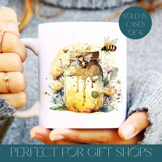 Ceramic white mug being held in hand with a honeypot and bees, text reads sold in cases of 6 and perfect for gift shops