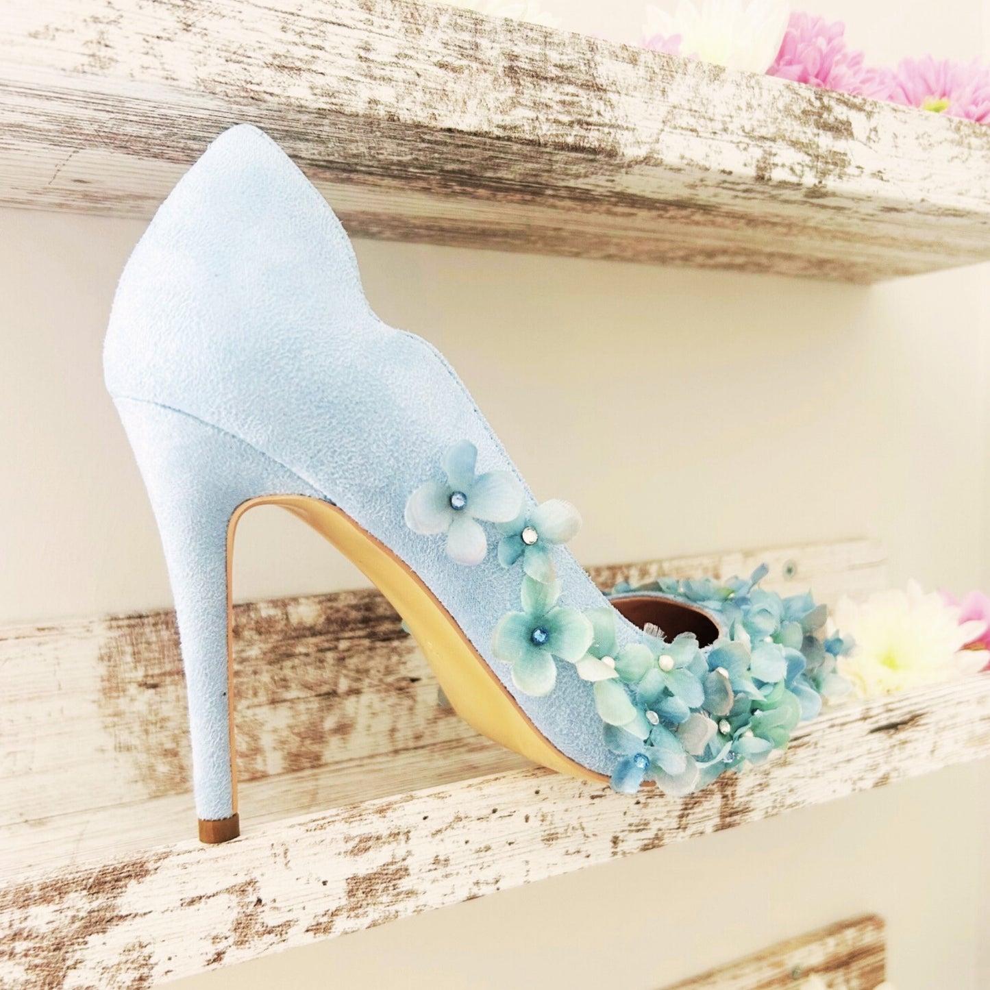 Light blue high-heeled shoe with floral decorations on a wooden surface