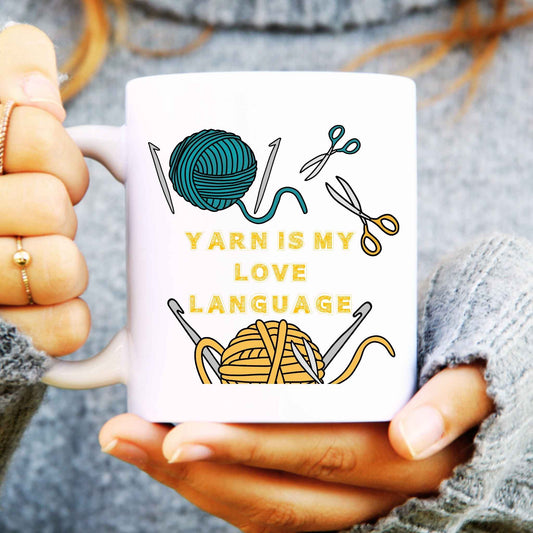 Person holding a mug with yarn-themed design and text 'Yarn is my love language'.